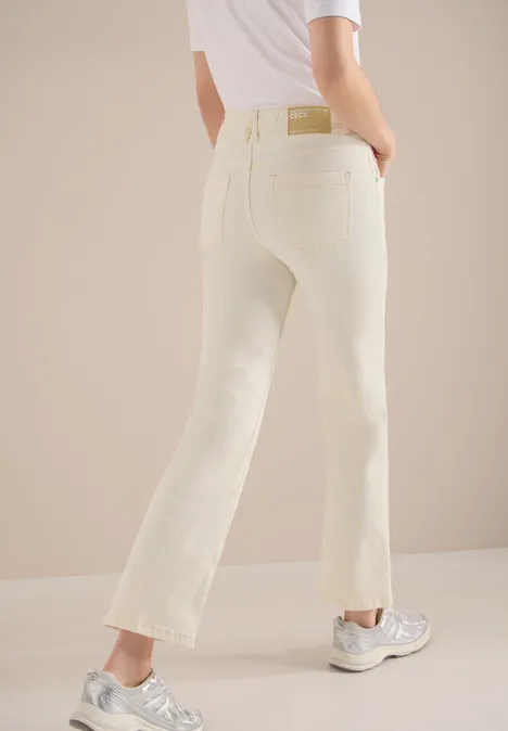 Cremefarbene Jeans mit geradem Bein, kombiniert mit silbernen Sneakern vor hellem Hintergrund.
